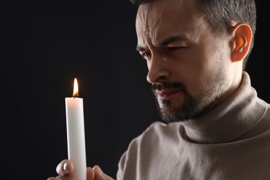 Sad man with burning candle crying on black background