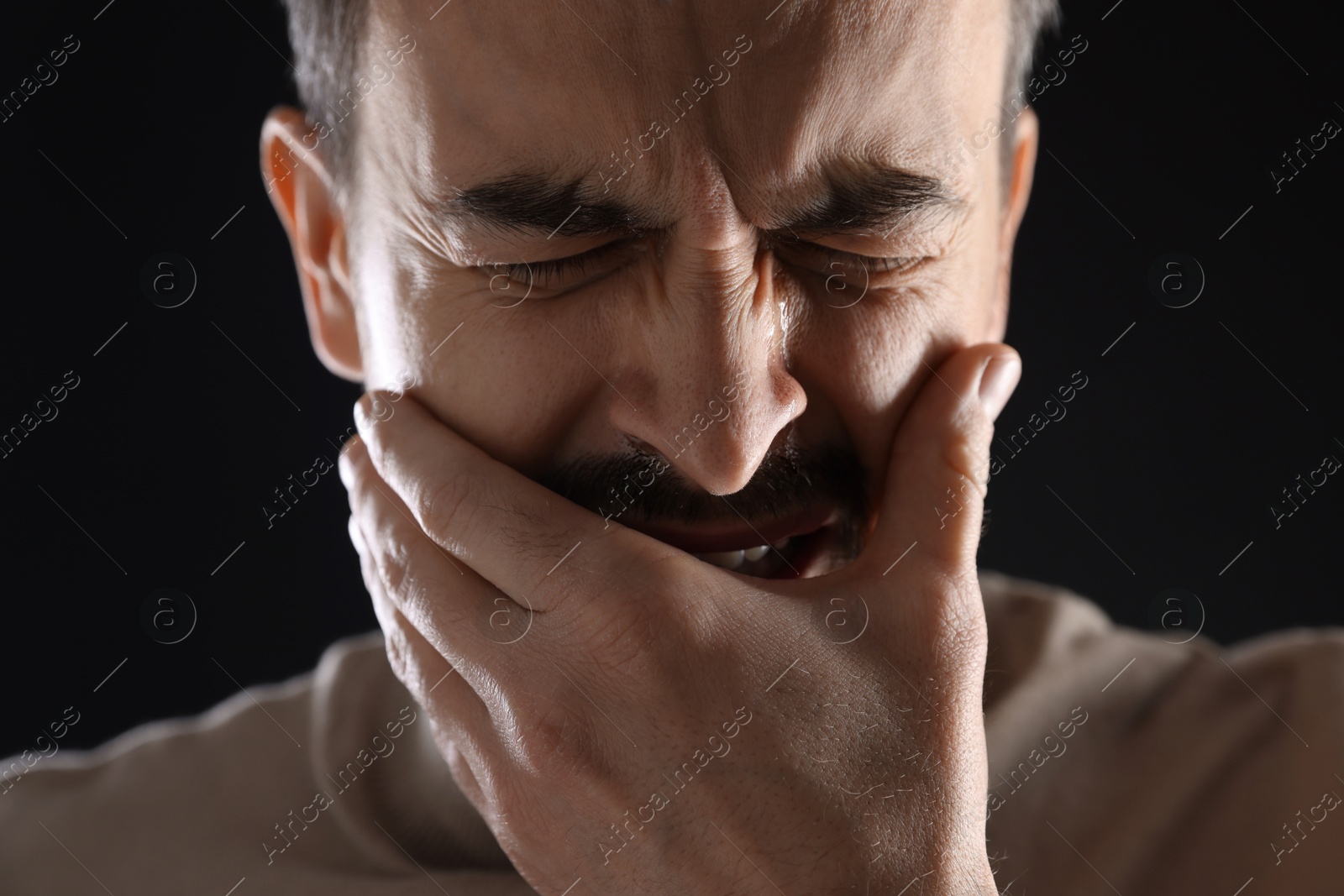 Photo of Sad man crying on black background, closeup