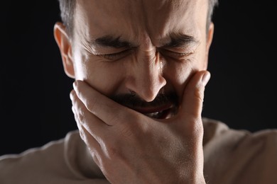 Photo of Sad man crying on black background, closeup