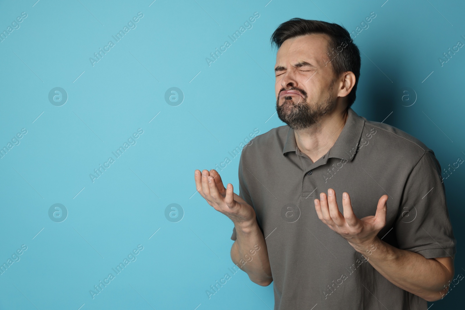 Photo of Sad man crying on light blue background, space for text