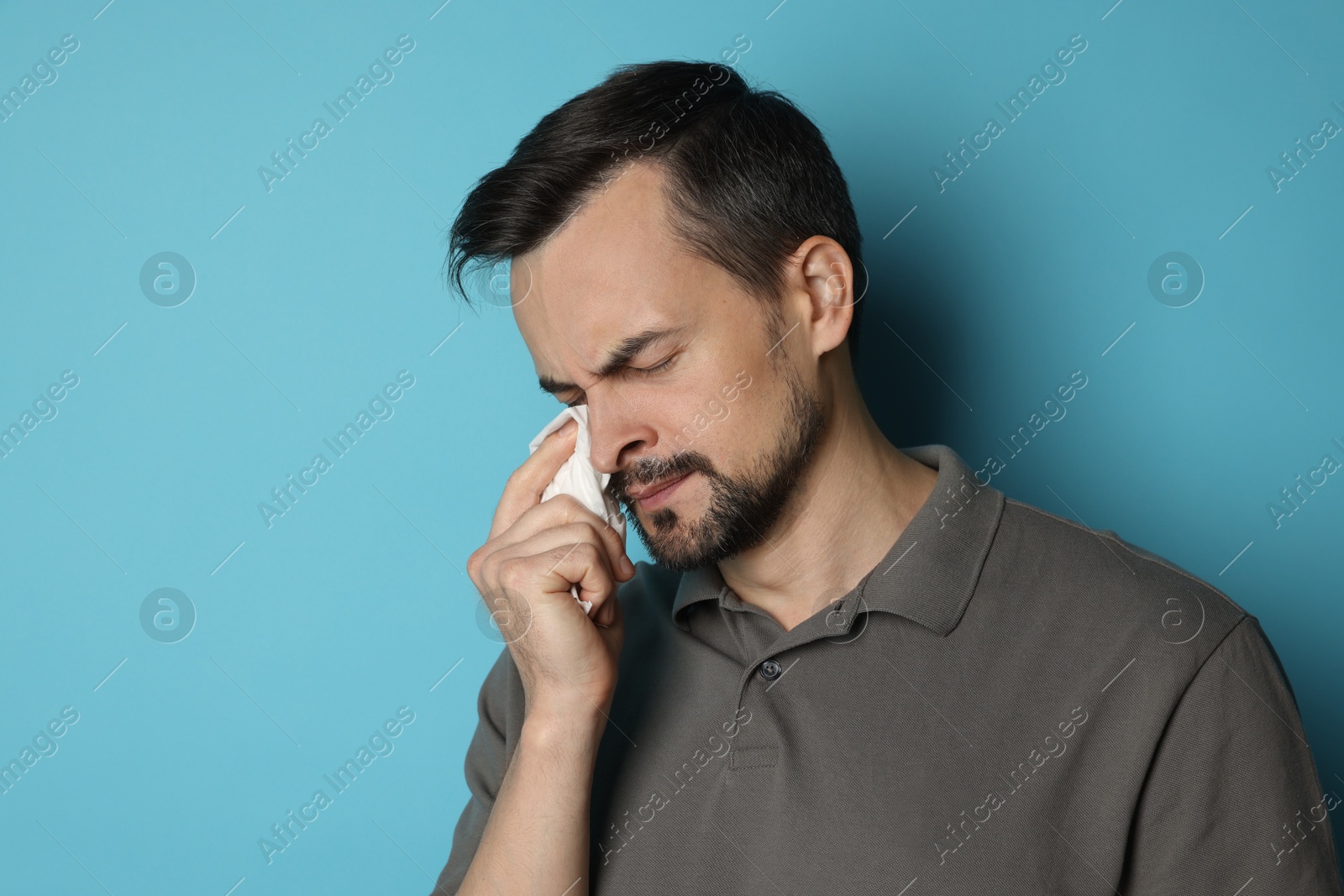 Photo of Sad man with paper tissue crying on light blue background