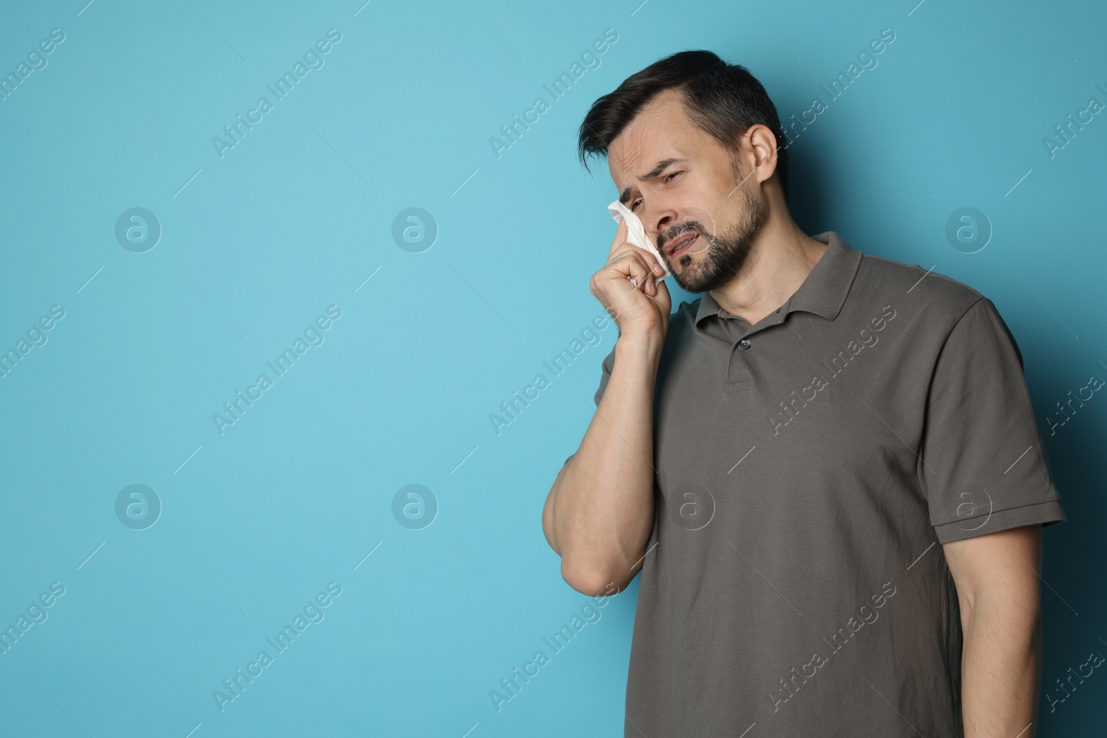 Photo of Sad man with paper tissue crying on light blue background, space for text