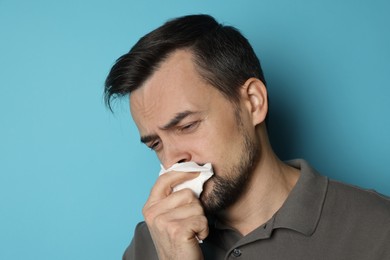 Photo of Sad man with paper tissue crying on light blue background