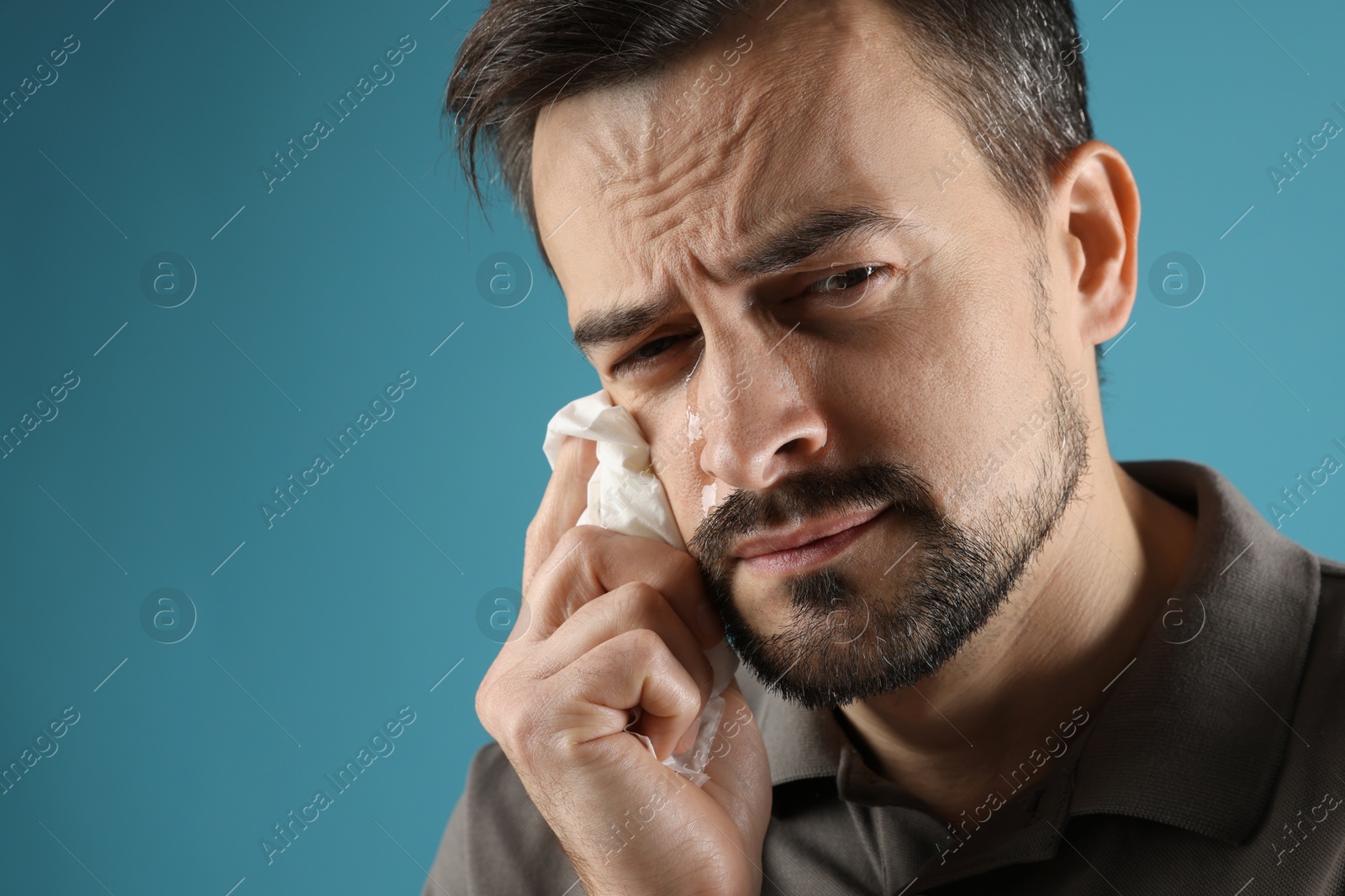 Photo of Sad man with paper tissue crying on light blue background, space for text