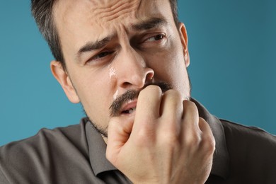 Photo of Sad man crying on light blue background, closeup