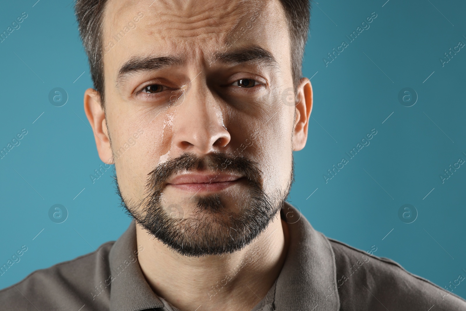 Photo of Sad man crying on light blue background, closeup