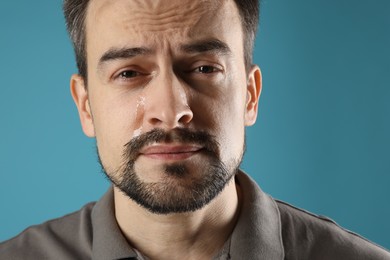 Photo of Sad man crying on light blue background, closeup