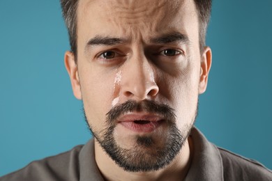 Photo of Sad man crying on light blue background, closeup