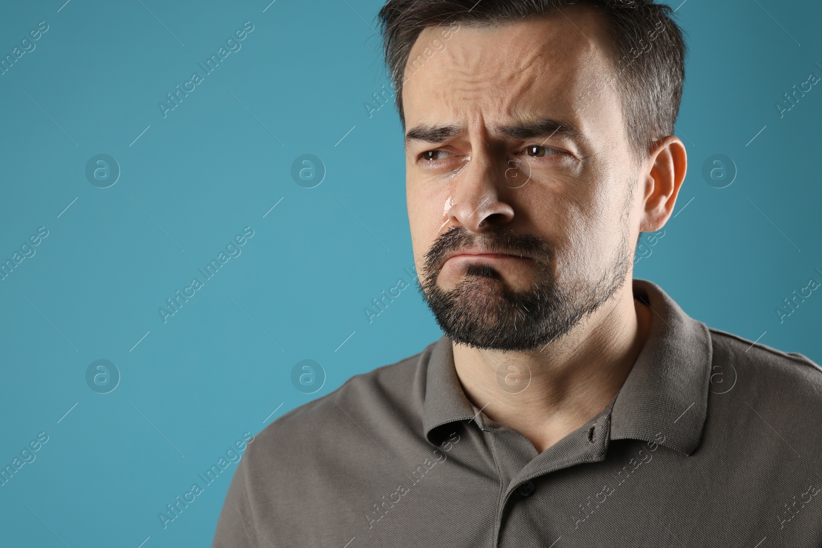 Photo of Sad man crying on light blue background, space for text