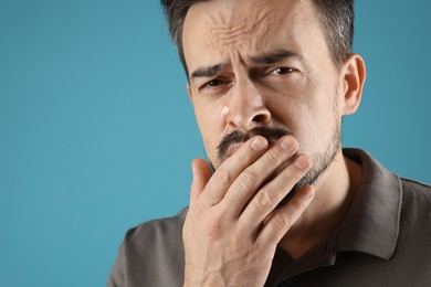 Photo of Sad man crying on light blue background, space for text