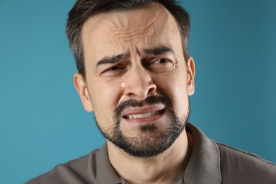 Sad man crying on light blue background, closeup