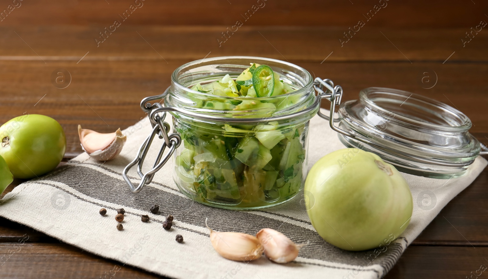 Photo of Delicious green salsa in jar and ingredients on wooden table