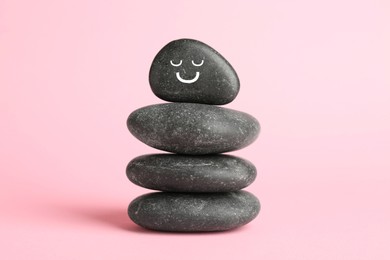 Photo of Stack of rocks with drawn smiley face on light pink background. Harmony and life balance