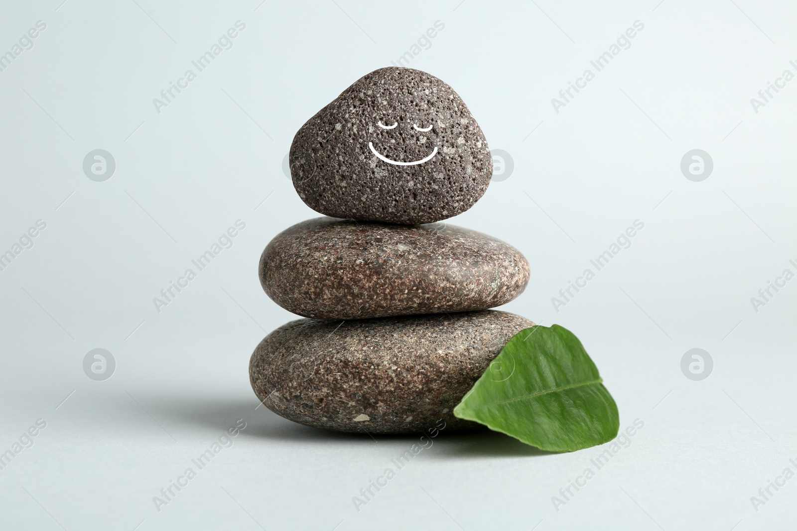 Photo of Stack of rocks with drawn smiley face on light grey background. Harmony and life balance