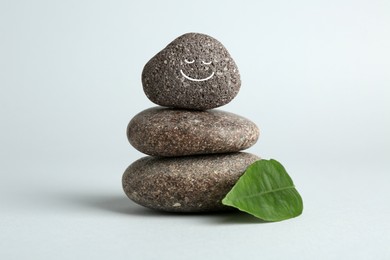 Photo of Stack of rocks with drawn smiley face on light grey background. Harmony and life balance