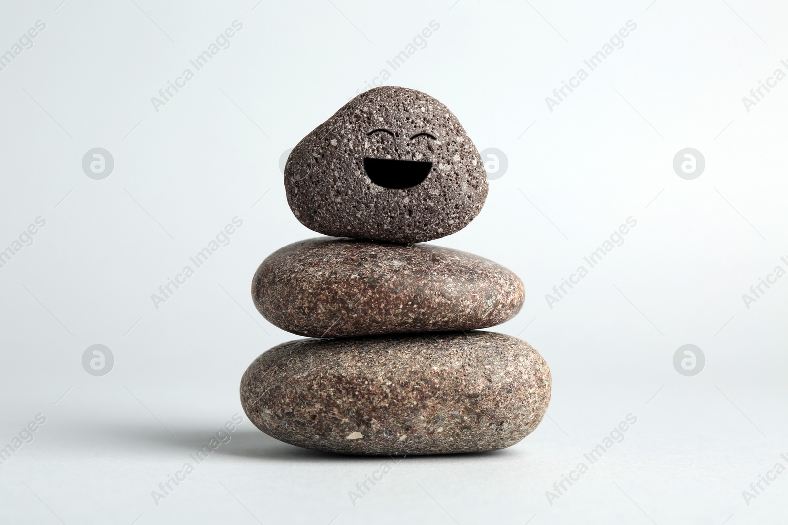 Photo of Stack of rocks with drawn smiley face on light grey background. Harmony and life balance