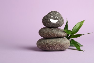 Photo of Stack of rocks with drawn smiley face on lilac background, space for text. Harmony and life balance