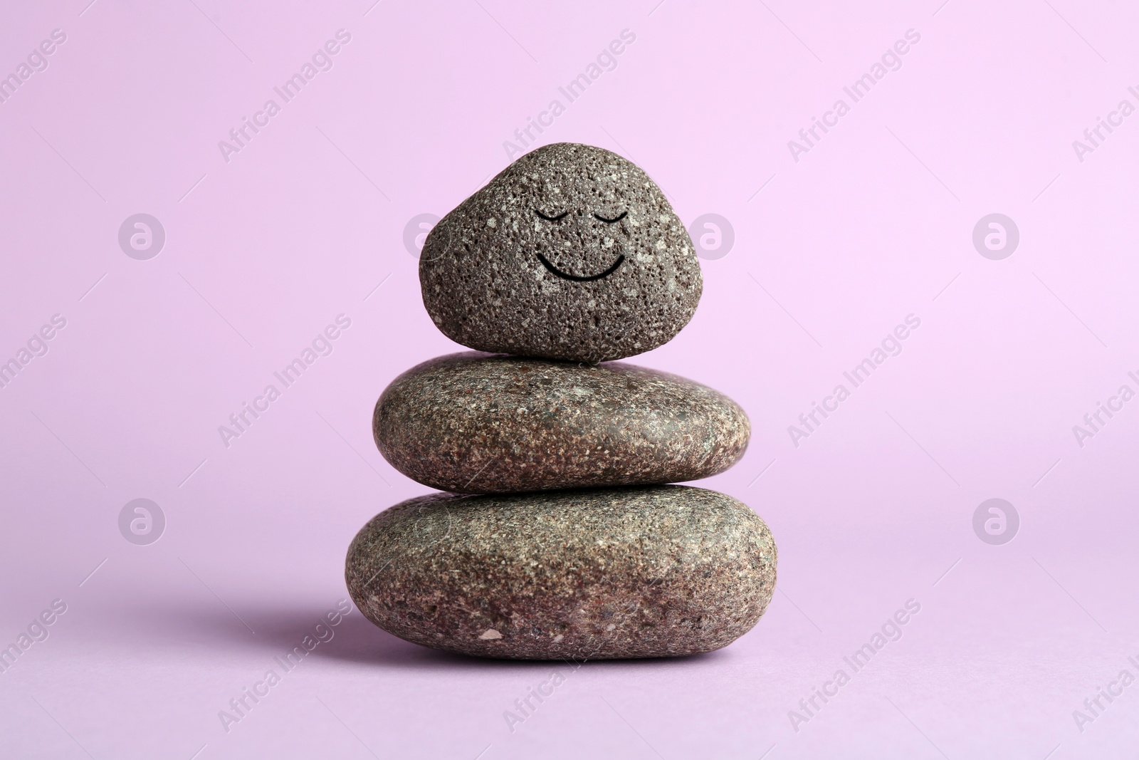 Photo of Stack of rocks with drawn smiley face on lilac background. Harmony and life balance