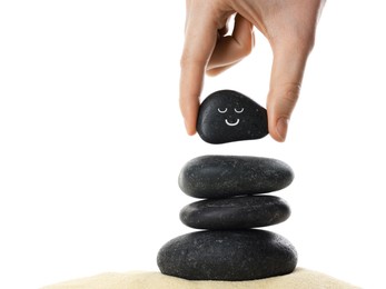 Photo of Woman putting stone with drawn smiley face on stack against white background, closeup. Harmony and life balance