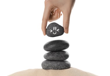 Photo of Woman putting stone with drawn smiley face on stack against white background, closeup. Harmony and life balance