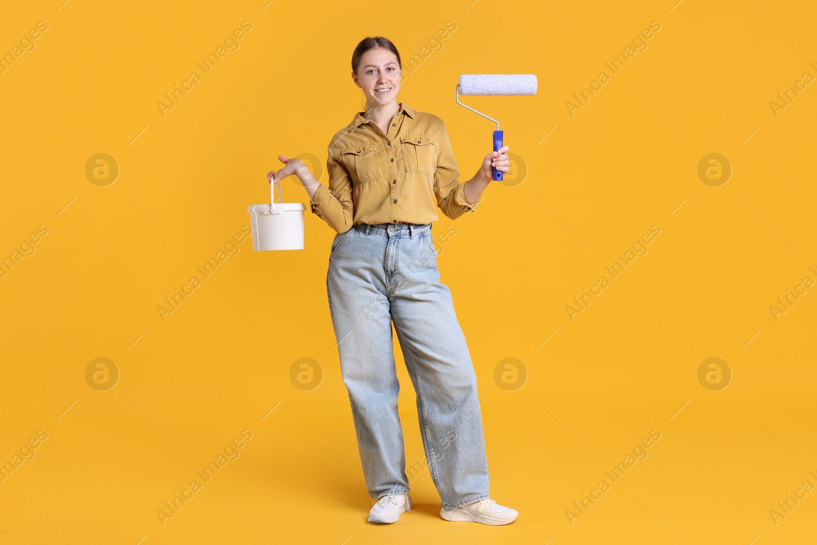 Photo of Woman with roller and bucket of paint on orange background