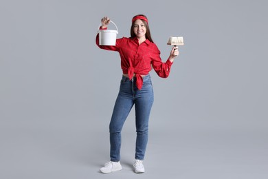 Woman with brush and bucket of paint on light grey background