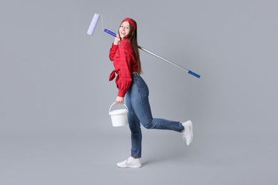 Photo of Woman with roller and bucket of paint on light grey background