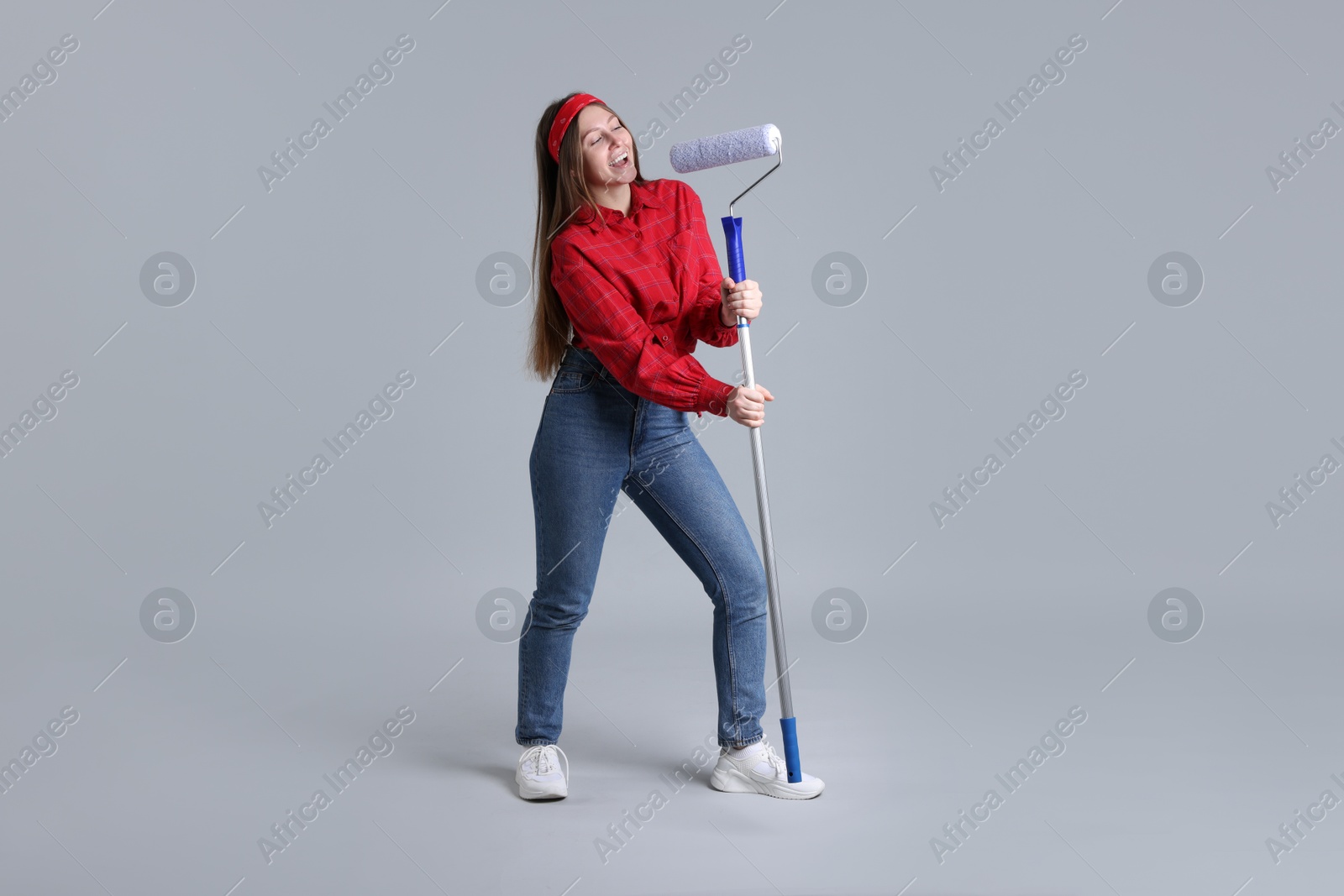 Photo of Woman with paint roller having fun on light grey background