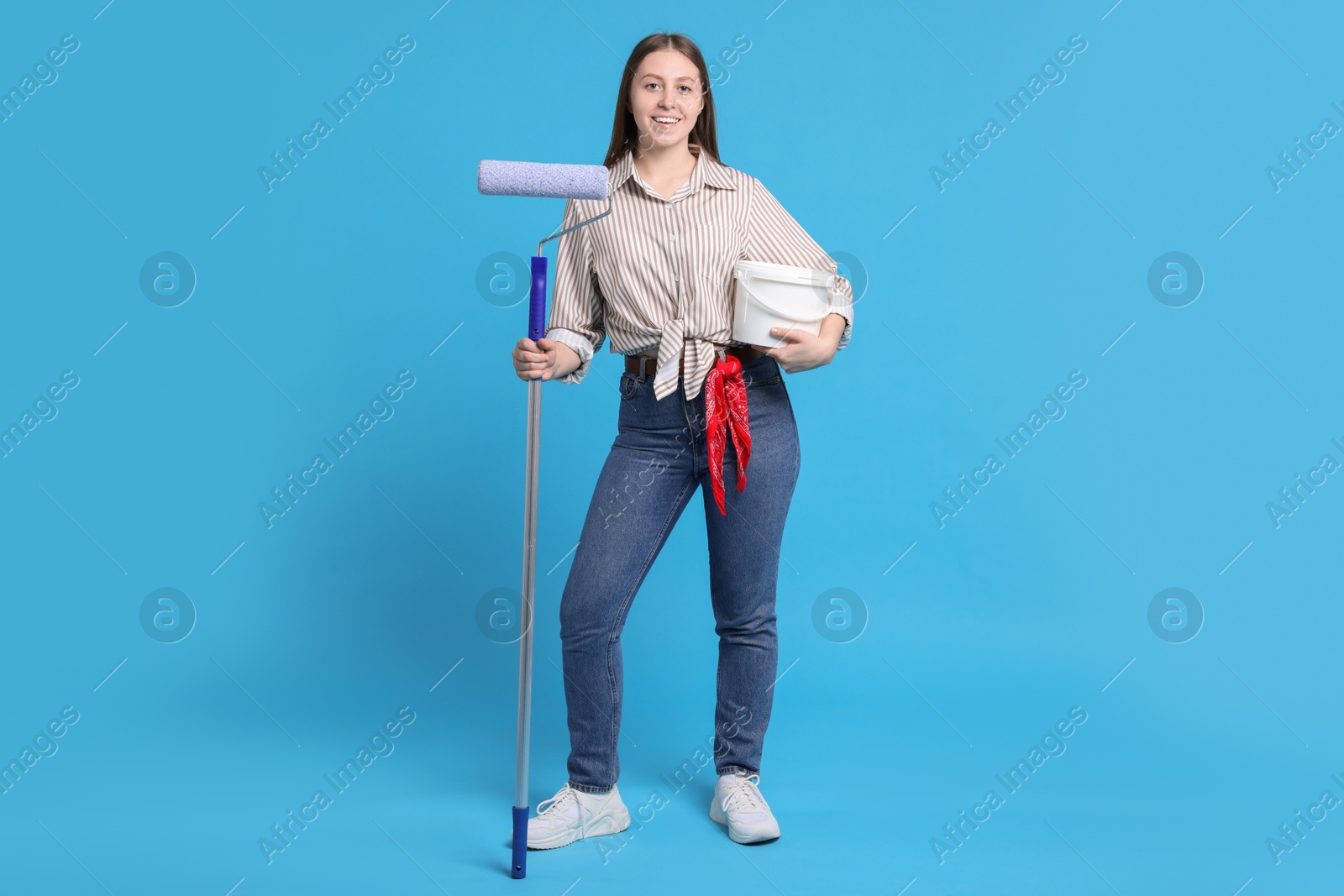 Photo of Woman with roller and bucket of paint on light blue background