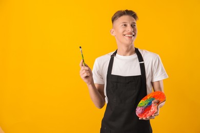 Photo of Smiling man with palette and paintbrush on orange background. Space for text