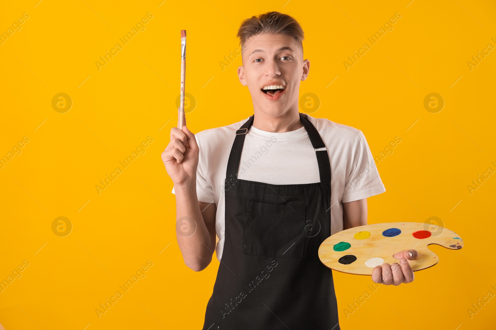 Photo of Emotional man with wooden palette and paintbrush on orange background. Space for text