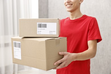 Photo of Man holding parcels with shipping labels indoors, closeup