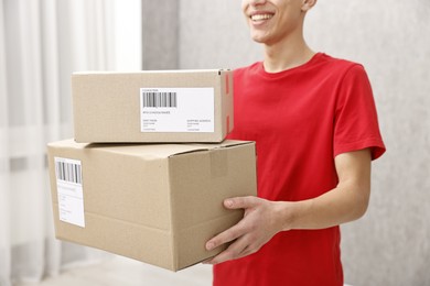 Photo of Man holding parcels with shipping labels indoors, closeup