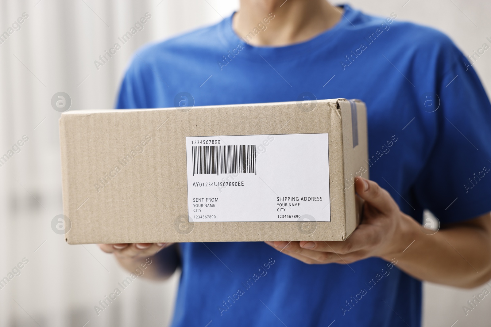 Photo of Man holding parcel with shipping label indoors, closeup