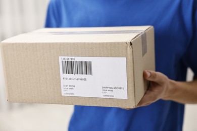 Photo of Man holding parcel with shipping label indoors, closeup