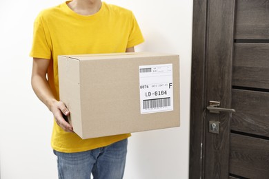 Photo of Man holding parcel with shipping label near door indoors, closeup. Space for text