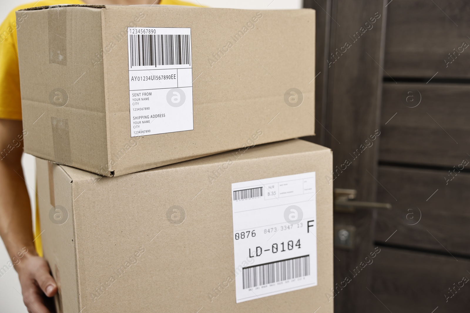 Photo of Man holding parcels with shipping labels near door indoors, closeup. Space for text