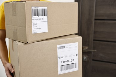 Man holding parcels with shipping labels near door indoors, closeup. Space for text