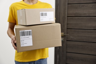 Man holding parcels with shipping labels near door indoors, closeup. Space for text