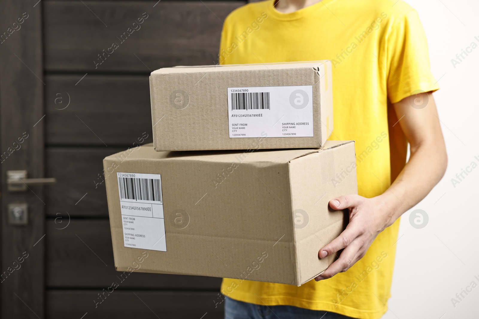 Photo of Man holding parcels with shipping labels near door indoors, closeup