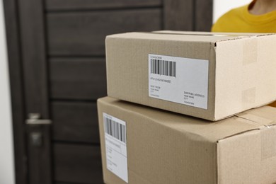 Photo of Man holding parcels with shipping labels near door indoors, closeup. Space for text