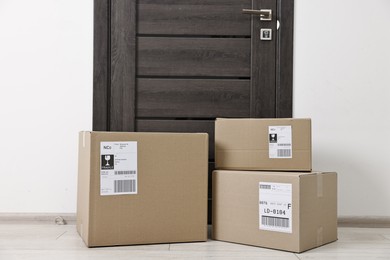 Photo of Cardboard parcel boxes with shipping labels near door indoors