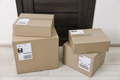 Photo of Cardboard parcel boxes with shipping labels near door indoors