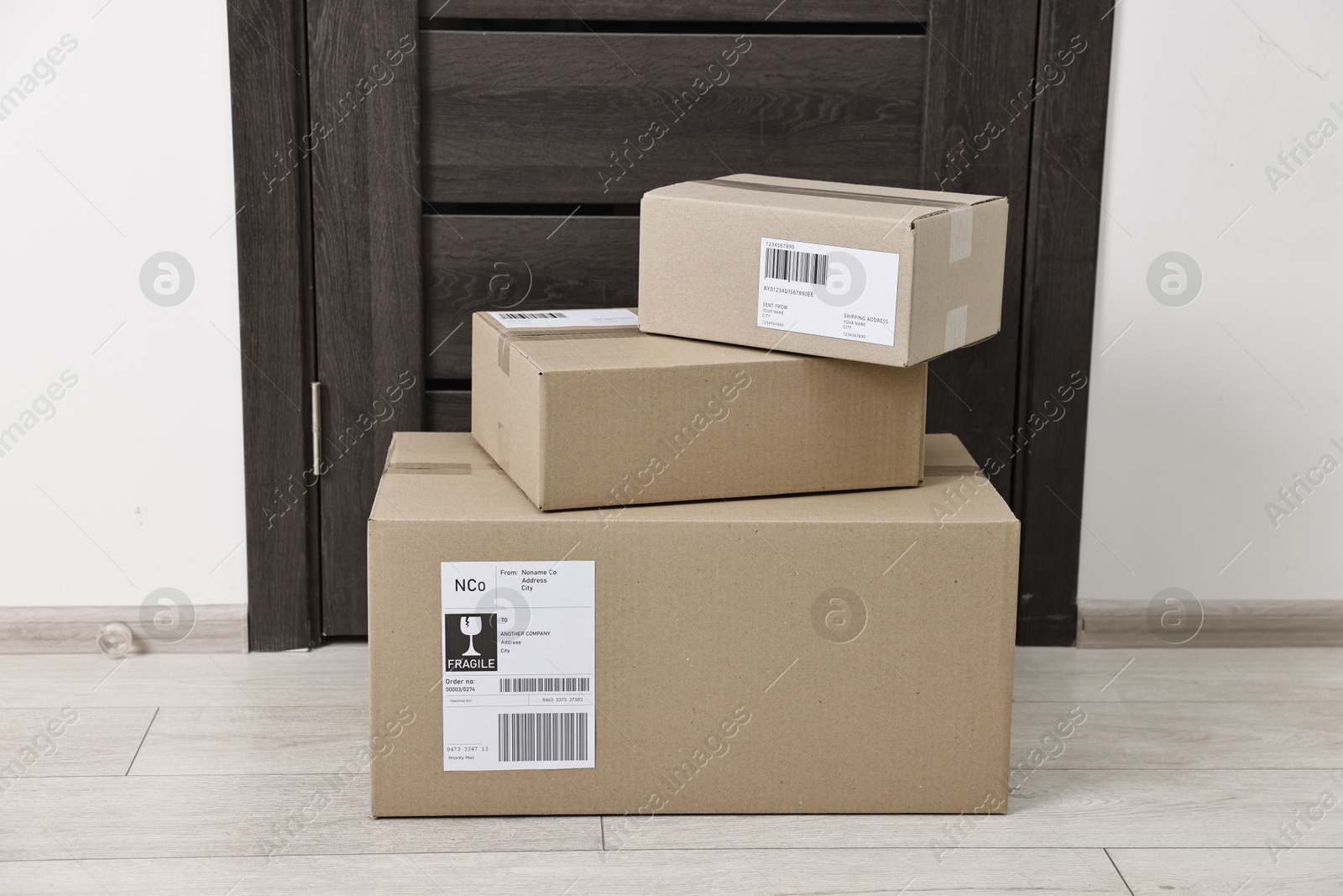 Photo of Cardboard parcel boxes with shipping labels near door indoors