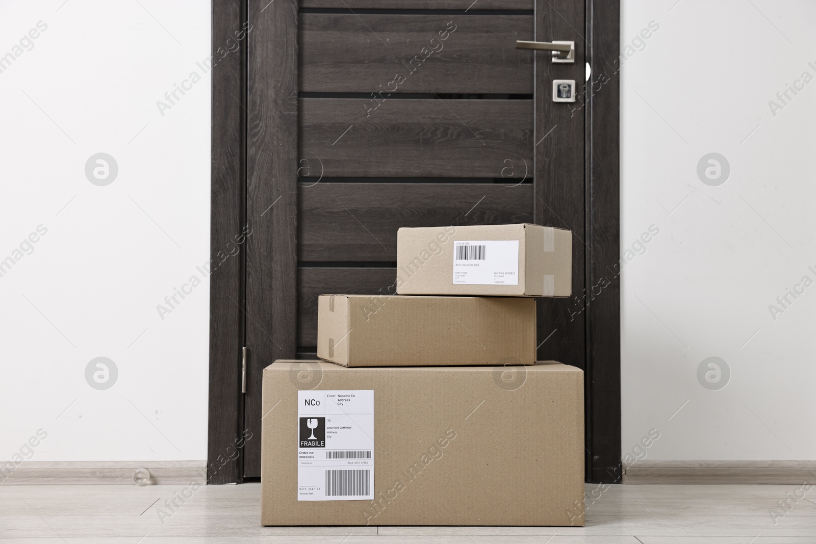 Photo of Cardboard parcel boxes with shipping labels near door indoors