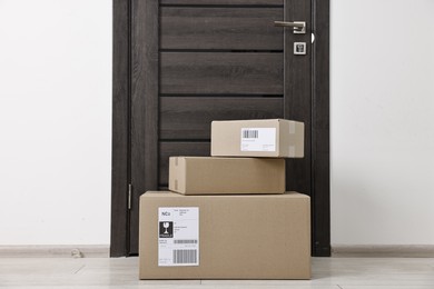 Photo of Cardboard parcel boxes with shipping labels near door indoors