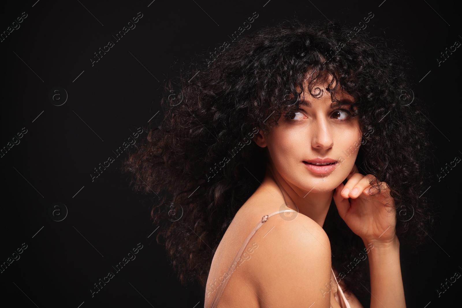 Photo of Beautiful young woman with long curly hair on black background. Space for text