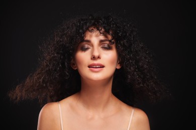 Photo of Beautiful young woman with long curly hair on black background