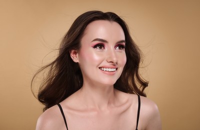 Photo of Portrait of beautiful young woman with stylish makeup and gorgeous hair on beige background