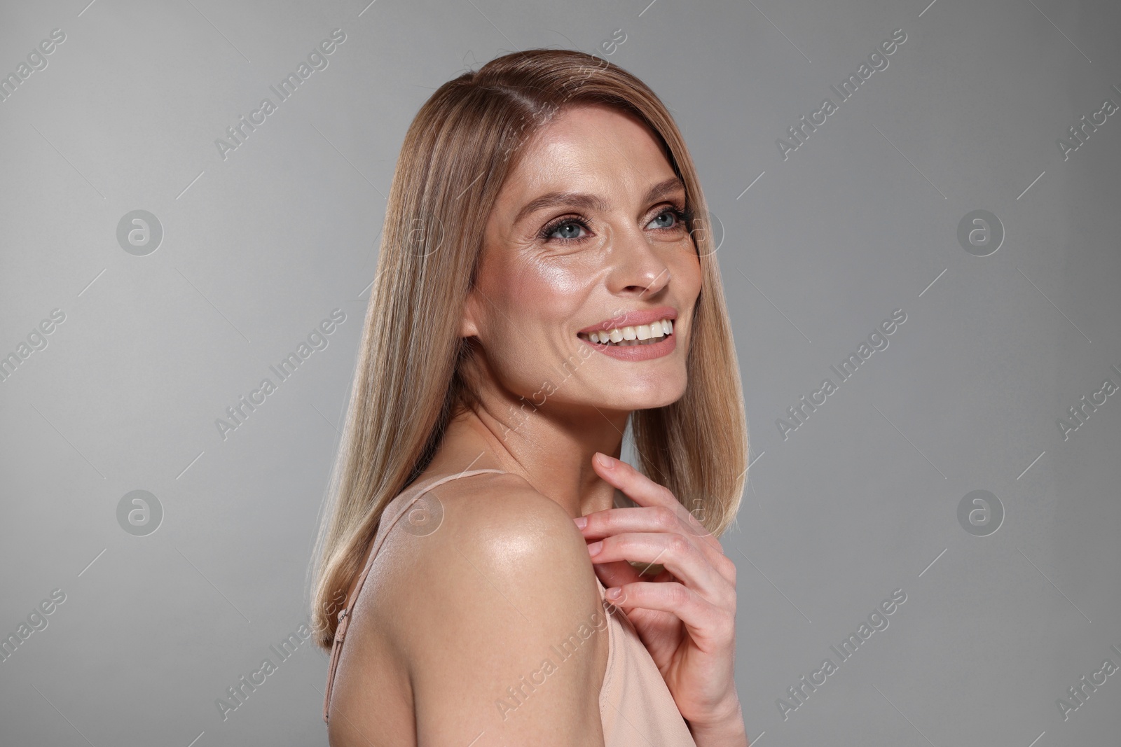 Photo of Portrait of beautiful happy woman with straight blonde hair on grey background